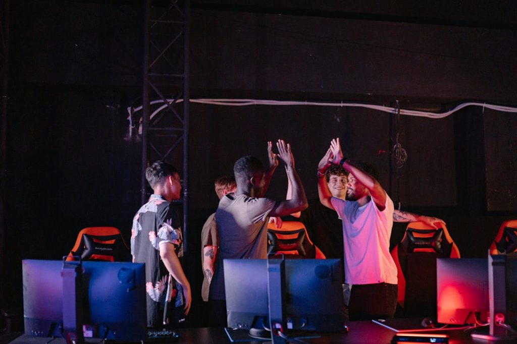 A diverse group of young gamers celebrating a victory with high-fives in a dark gaming room.